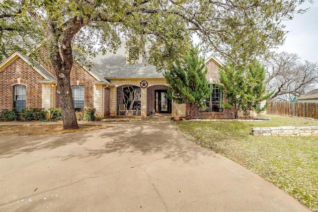 view of front facade with concrete driveway, roof with shingles, fence, french doors, and brick siding