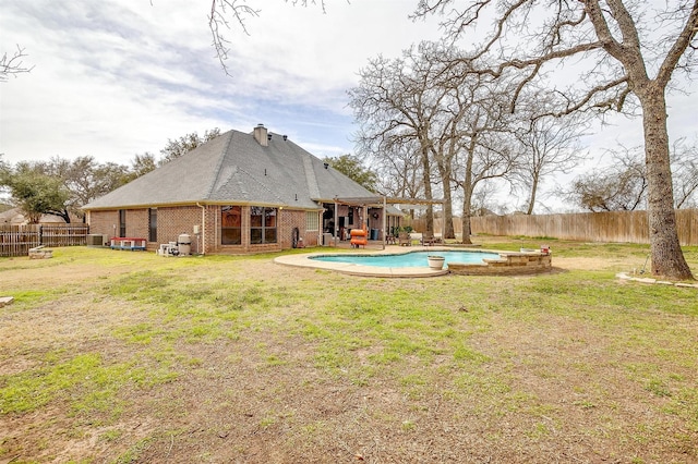 rear view of house featuring a fenced in pool, a fenced backyard, a chimney, a yard, and brick siding