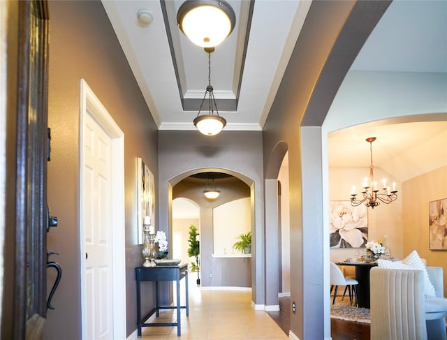 hallway with baseboards, arched walkways, ornamental molding, a raised ceiling, and tile patterned floors