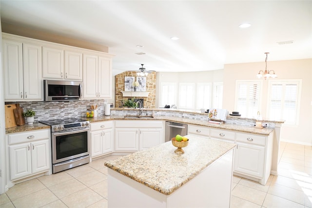 kitchen with a peninsula, a sink, stainless steel appliances, ceiling fan with notable chandelier, and tasteful backsplash