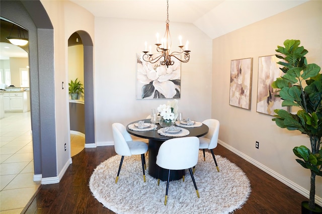 dining area featuring arched walkways, lofted ceiling, baseboards, and wood finished floors