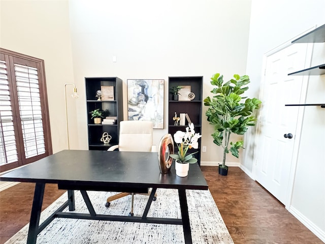 office area featuring baseboards, a towering ceiling, and dark wood-style flooring