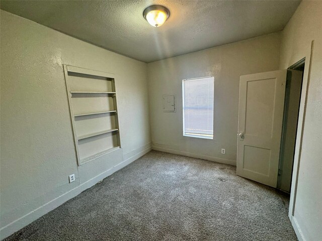 carpeted spare room featuring built in features, a textured wall, a textured ceiling, and baseboards