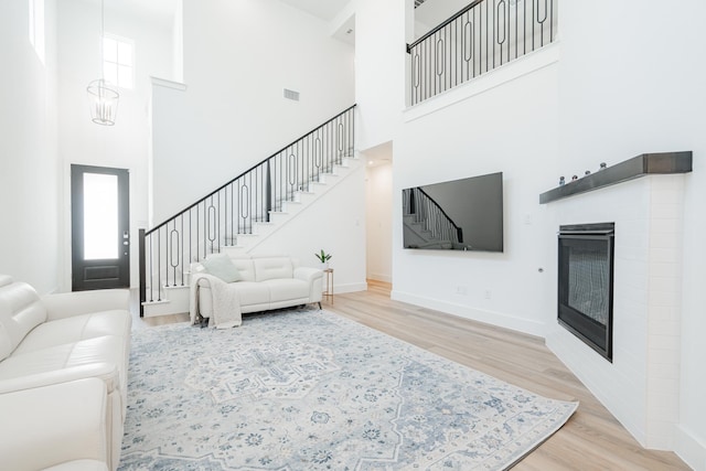 living area featuring stairs, a glass covered fireplace, wood finished floors, and visible vents