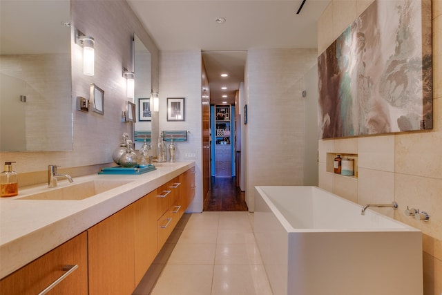 full bath with a soaking tub, tile patterned flooring, tile walls, and a sink