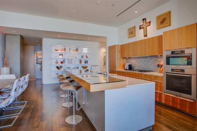 kitchen with an island with sink, a sink, dark wood finished floors, and stainless steel double oven