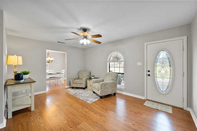 foyer featuring light wood-type flooring, baseboards, visible vents, and ceiling fan with notable chandelier