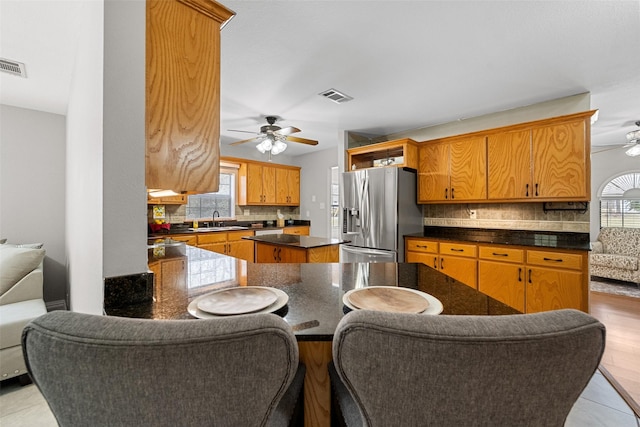 kitchen featuring a center island, visible vents, backsplash, a ceiling fan, and stainless steel fridge with ice dispenser