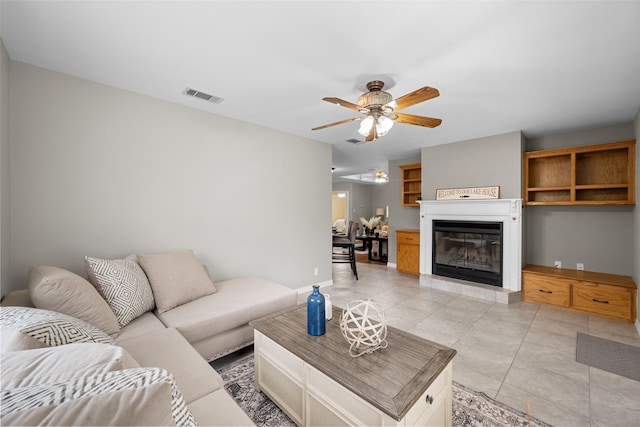 living room featuring light tile patterned floors, visible vents, baseboards, a ceiling fan, and a glass covered fireplace