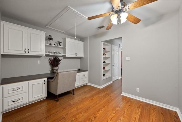 unfurnished office featuring wood finished floors, visible vents, baseboards, built in desk, and attic access