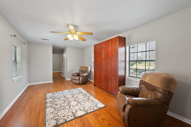 living area with visible vents, a ceiling fan, light wood-style flooring, and baseboards