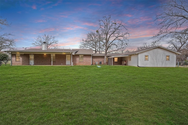 back of property at dusk with a chimney, a lawn, and brick siding