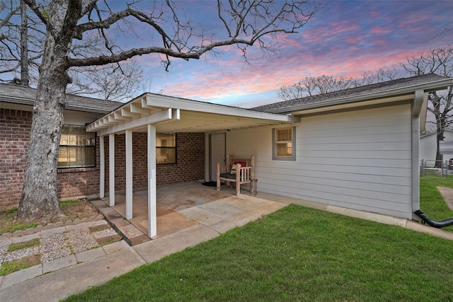 back of property with a carport, a patio area, brick siding, and a lawn