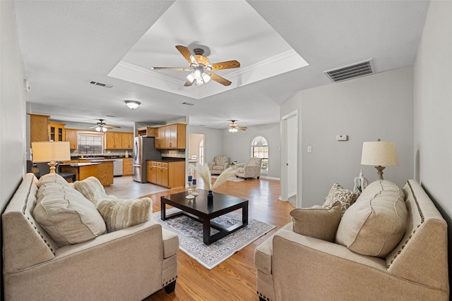 living room with ornamental molding, a raised ceiling, visible vents, and light wood-style flooring