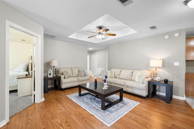 living room with a tray ceiling, light wood-type flooring, visible vents, and a ceiling fan