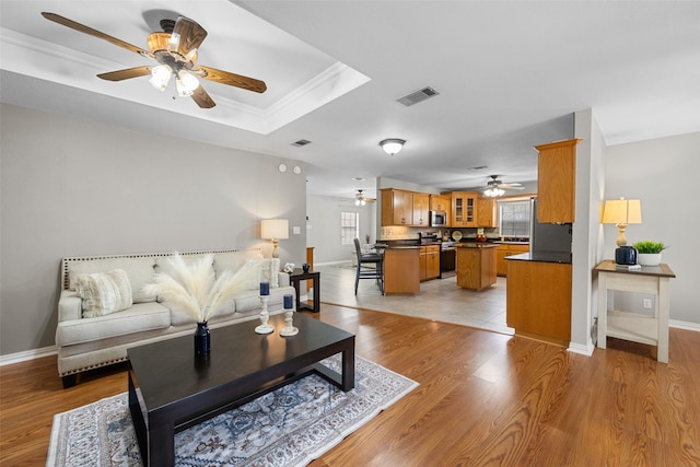 living area with ornamental molding, light wood-type flooring, visible vents, and baseboards