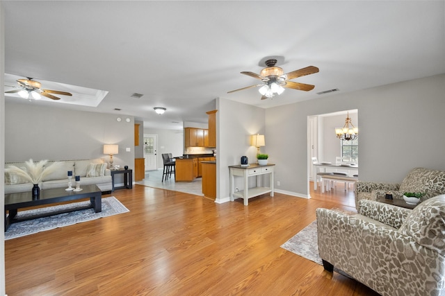 living area featuring light wood-style floors, baseboards, visible vents, and ceiling fan with notable chandelier