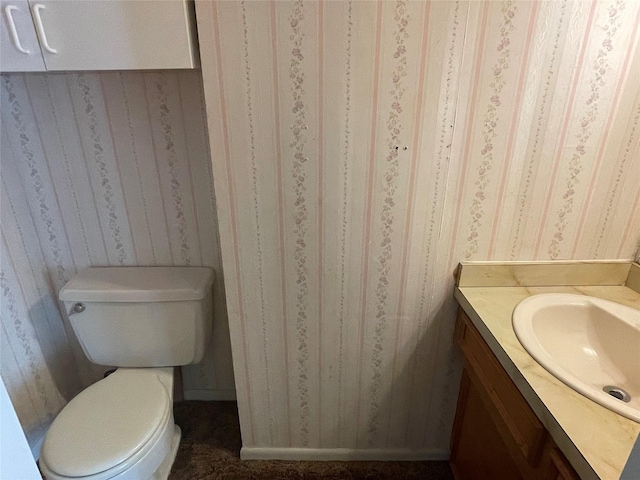 bathroom featuring toilet, wallpapered walls, baseboards, and vanity