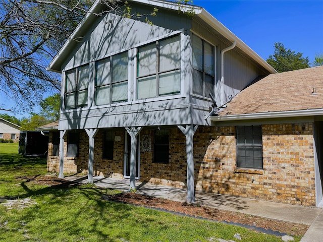 view of front of home featuring brick siding, a shingled roof, and a front yard