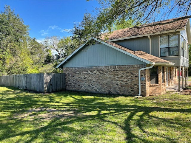 view of property exterior with brick siding, a lawn, and fence