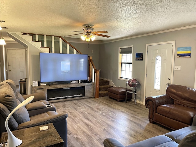 living area with a textured ceiling, wood finished floors, a ceiling fan, stairway, and crown molding