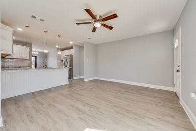 unfurnished living room with a ceiling fan, light wood-type flooring, visible vents, and baseboards