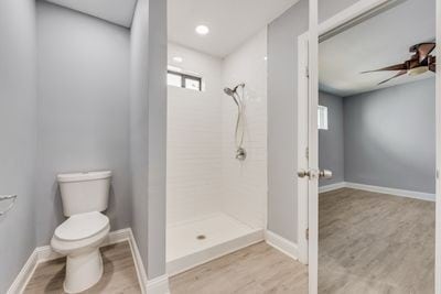 full bathroom featuring toilet, baseboards, tiled shower, and wood finished floors