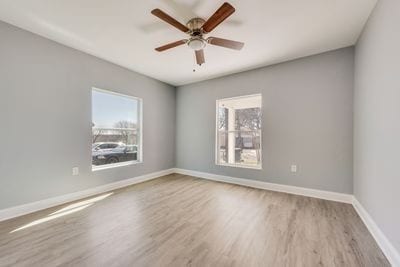 spare room featuring baseboards, ceiling fan, wood finished floors, and a healthy amount of sunlight