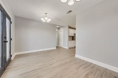 spare room featuring a chandelier, light wood-type flooring, visible vents, and baseboards