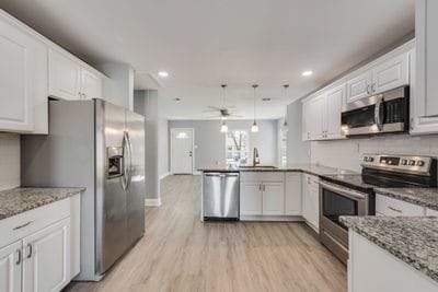 kitchen featuring stainless steel appliances, a peninsula, a sink, and white cabinetry