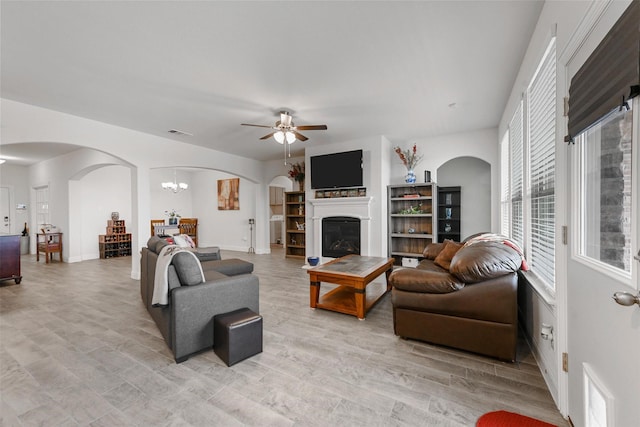 3512 Tunnel Ave, Aubrey, TX 76227 - living area with arched walkways, a ceiling fan, light wood finished floors, a glass covered fireplace, and a chandelier