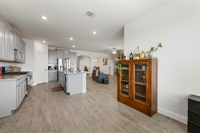 3512 Tunnel Ave, Aubrey, TX 76227 - kitchen with stainless steel appliances, arched walkways, gray cabinets, open floor plan, and light wood-style flooring