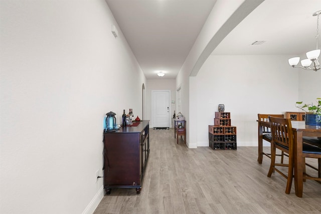 interior space with light wood finished floors, visible vents, arched walkways, baseboards, and a notable chandelier