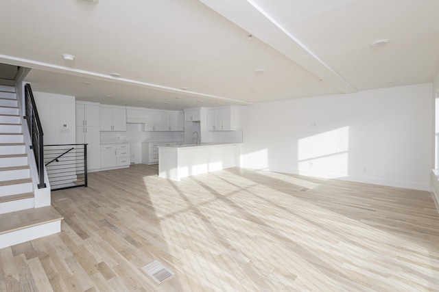 unfurnished living room with visible vents, light wood-style floors, a sink, baseboards, and stairs