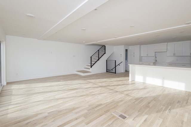 unfurnished living room featuring visible vents, light wood-style floors, a sink, baseboards, and stairs