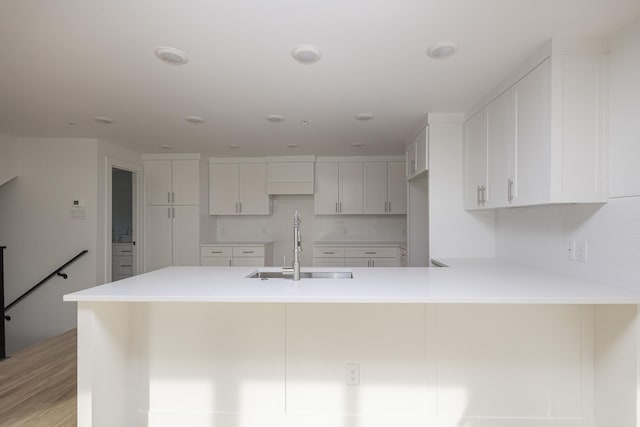 kitchen featuring white cabinets, decorative backsplash, a peninsula, light countertops, and a sink