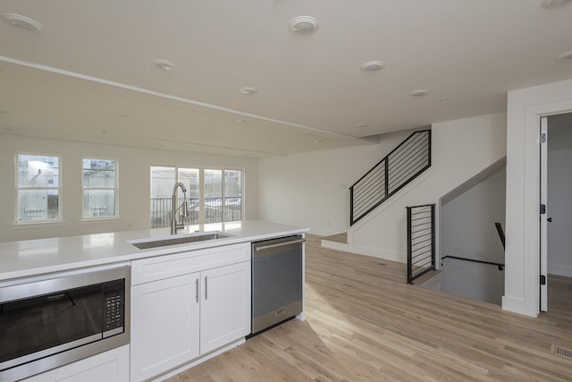 kitchen featuring a sink, white cabinetry, light countertops, appliances with stainless steel finishes, and light wood finished floors