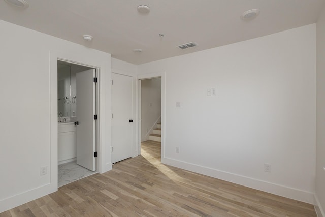 spare room featuring light wood-style floors, visible vents, a sink, and baseboards