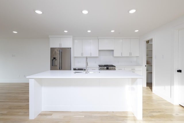 kitchen with high end refrigerator, a sink, white cabinets, light countertops, and range