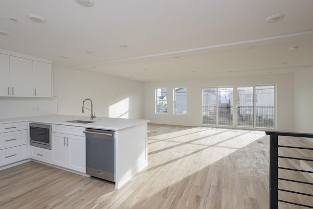 kitchen with open floor plan, a peninsula, stainless steel appliances, light wood-style floors, and a sink