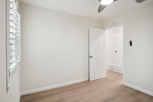 empty room with light wood finished floors, baseboards, a ceiling fan, and visible vents