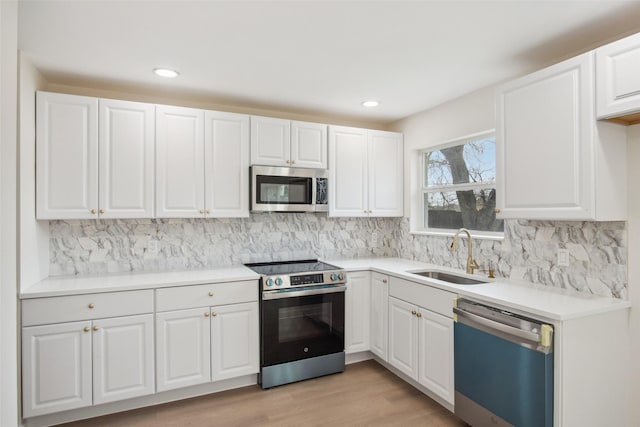 kitchen featuring tasteful backsplash, white cabinets, stainless steel appliances, light wood-style floors, and a sink