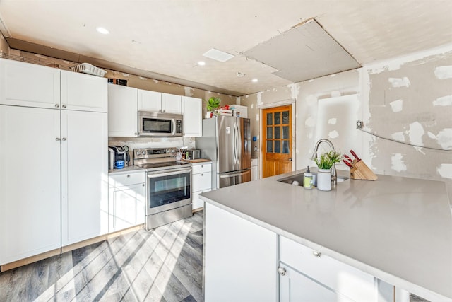 kitchen featuring stainless steel appliances, light countertops, white cabinets, a sink, and a peninsula