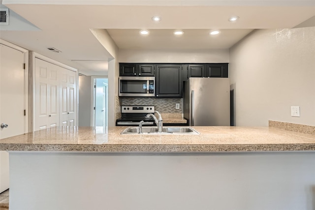 kitchen featuring tasteful backsplash, dark cabinets, stainless steel appliances, a sink, and recessed lighting