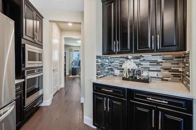 kitchen featuring backsplash, dark cabinetry, stainless steel appliances, and dark wood-type flooring