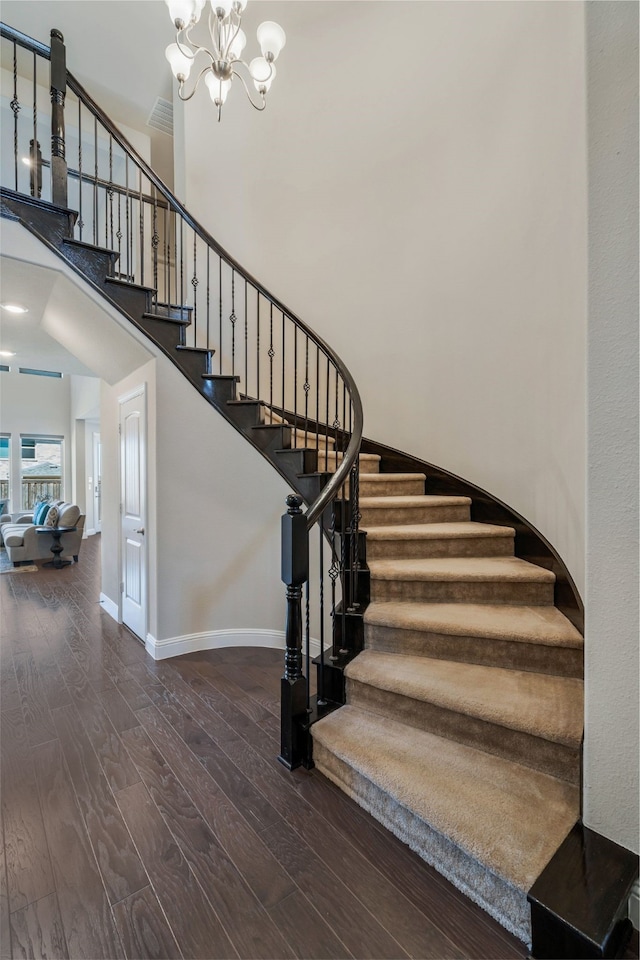 stairs with a chandelier, a high ceiling, wood finished floors, visible vents, and baseboards