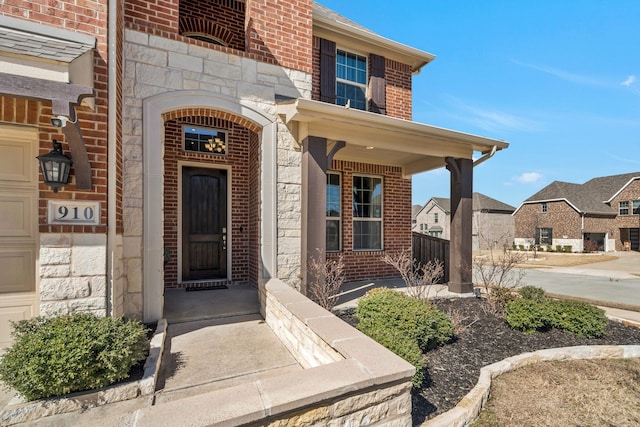 view of exterior entry featuring stone siding, brick siding, and covered porch