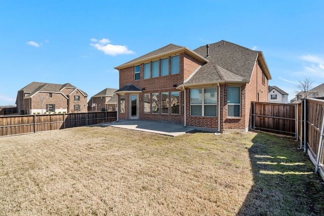 rear view of property with a lawn, a patio, a fenced backyard, roof with shingles, and brick siding