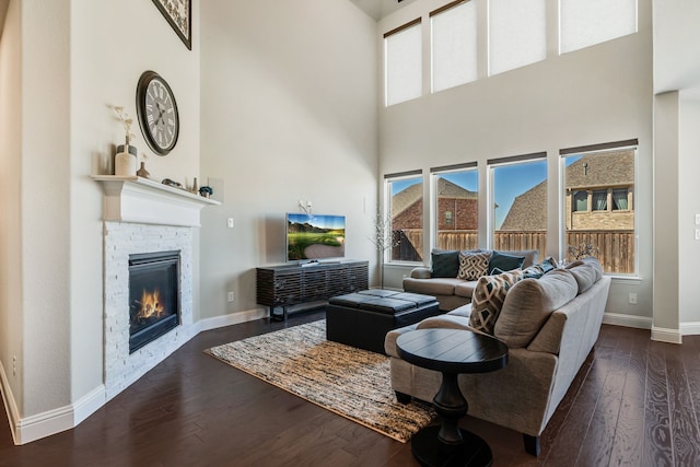 living room featuring a healthy amount of sunlight, dark wood-style floors, baseboards, and a stone fireplace