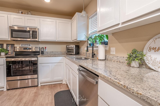 kitchen featuring stainless steel appliances, light wood-style flooring, white cabinetry, a sink, and light stone countertops